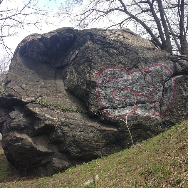 a large rock with graffiti on it is near some trees