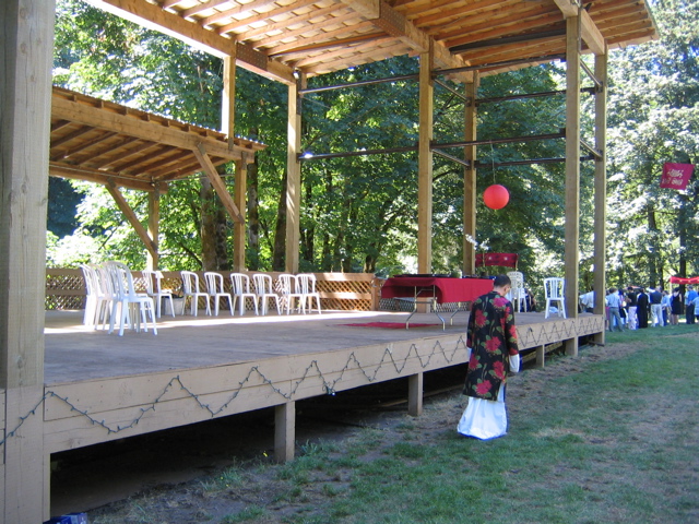 people are standing around a wooden structure as they walk toward an open area with white chairs