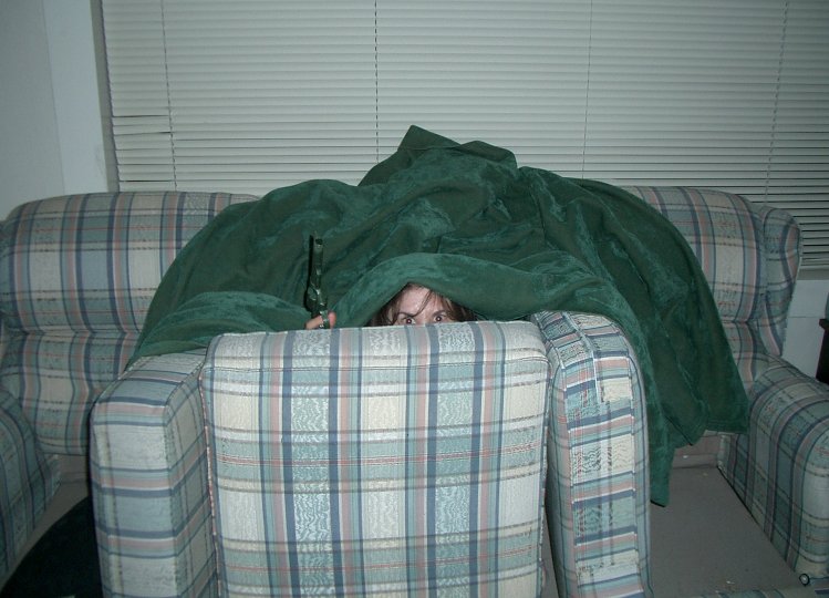 a girl hiding under a blanket behind a couch
