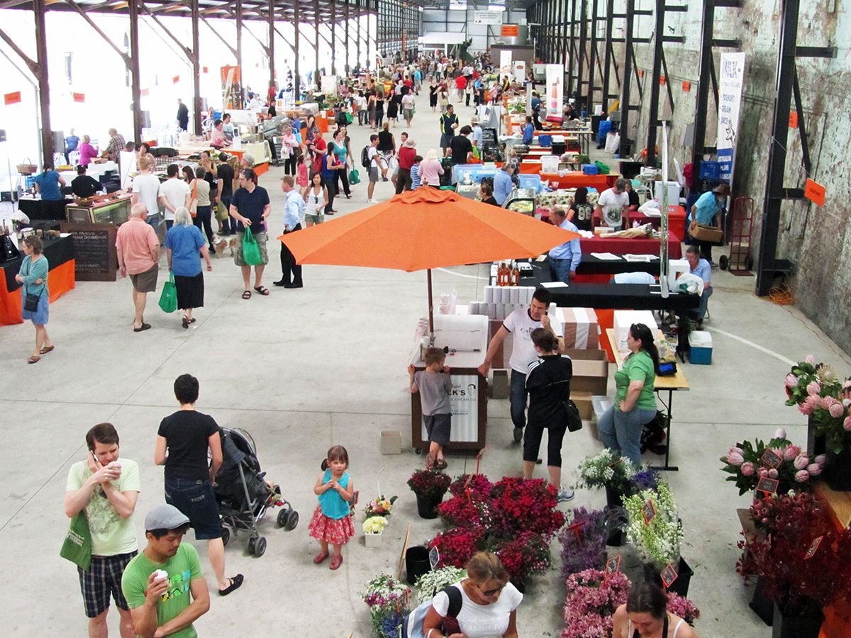 many people are at the farmers'market while some of them have an umbrella