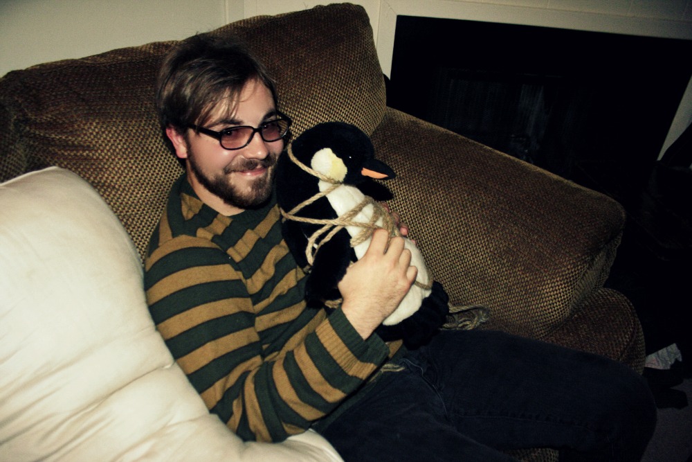 a man sits on a couch and holds a stuffed penguin