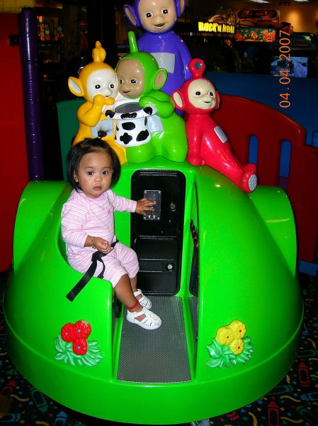 a child sits on a toy machine with some toys in the background