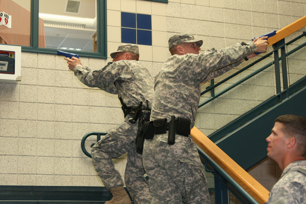 two men in uniform are holding guns in front of stairs