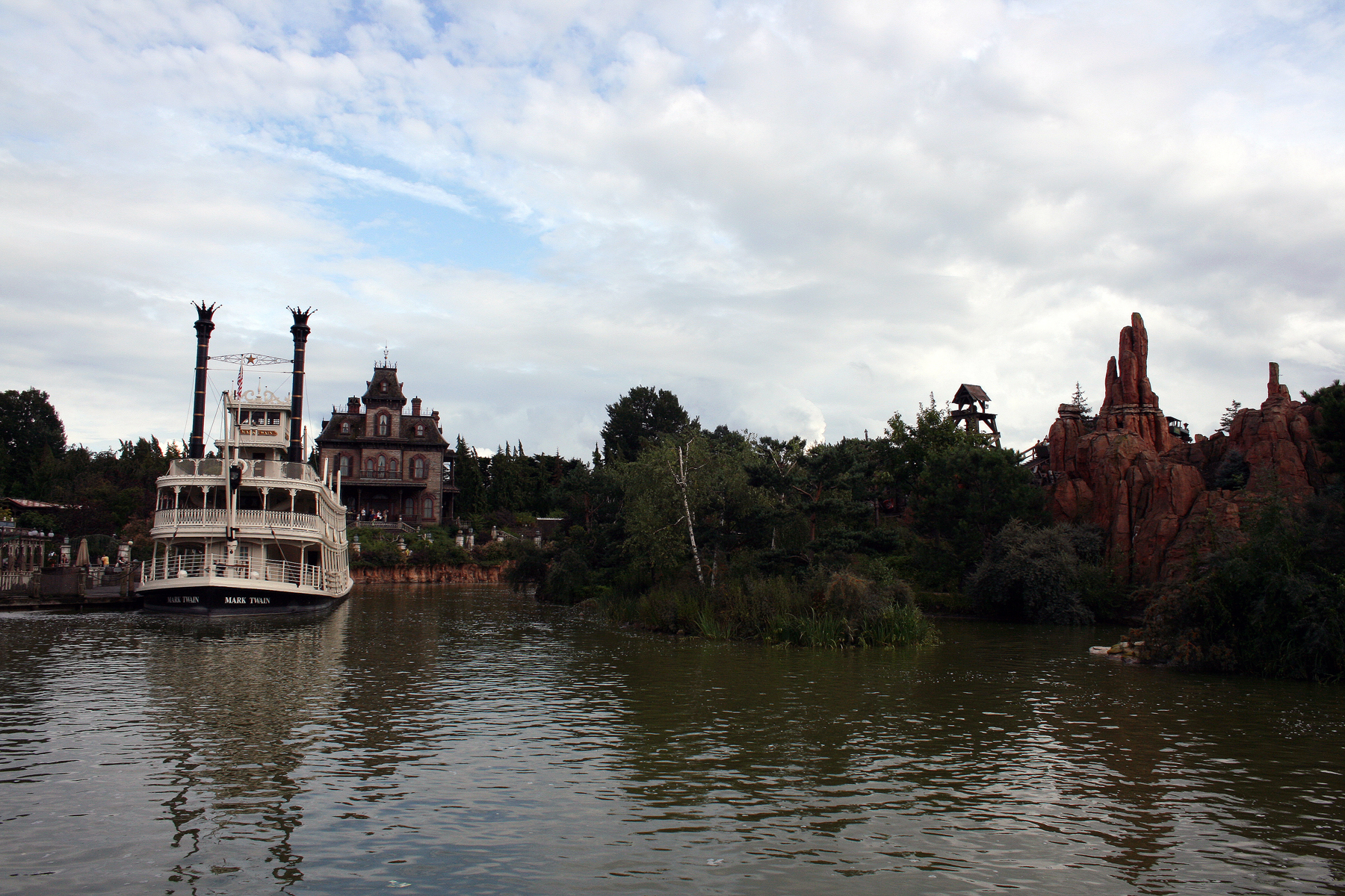 a house sitting on top of a river with lots of trees in front