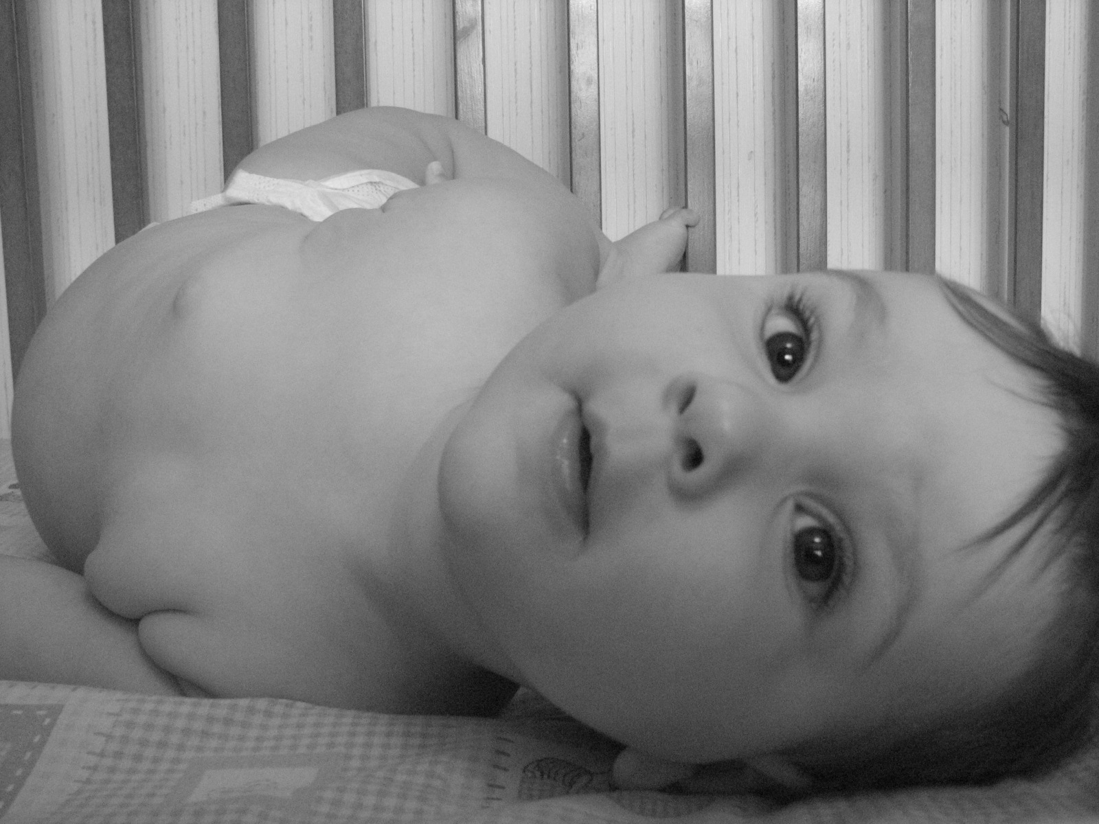 a baby laying on top of a bed next to a baby crib