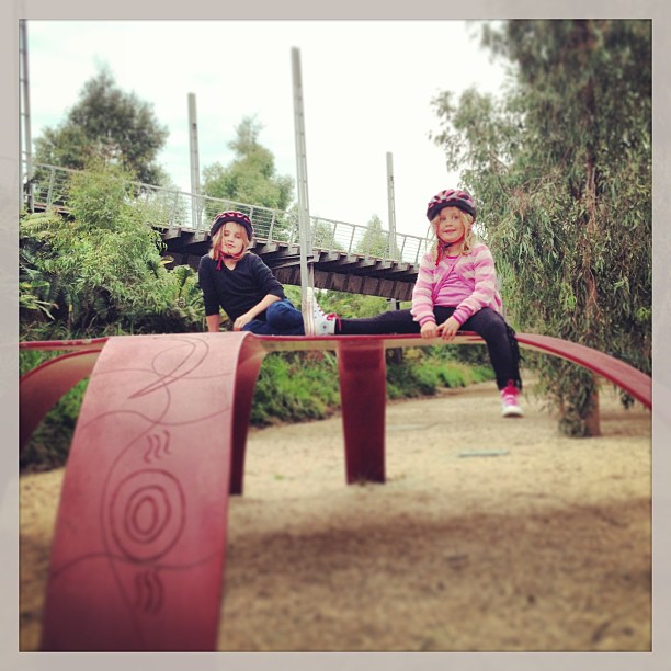 two girls are sitting on a playground rail