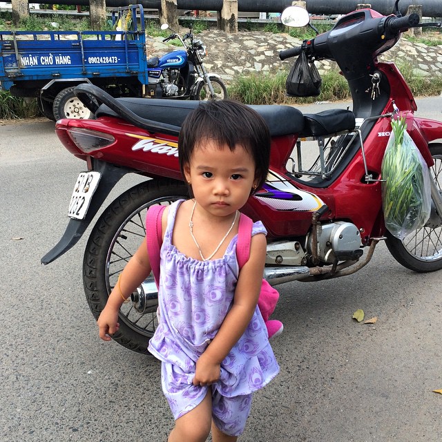 a little asian girl wearing a purple dress by her bike