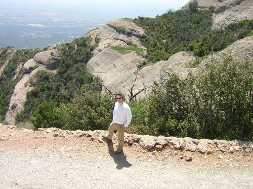 a man in white shirt standing on top of hill next to forest