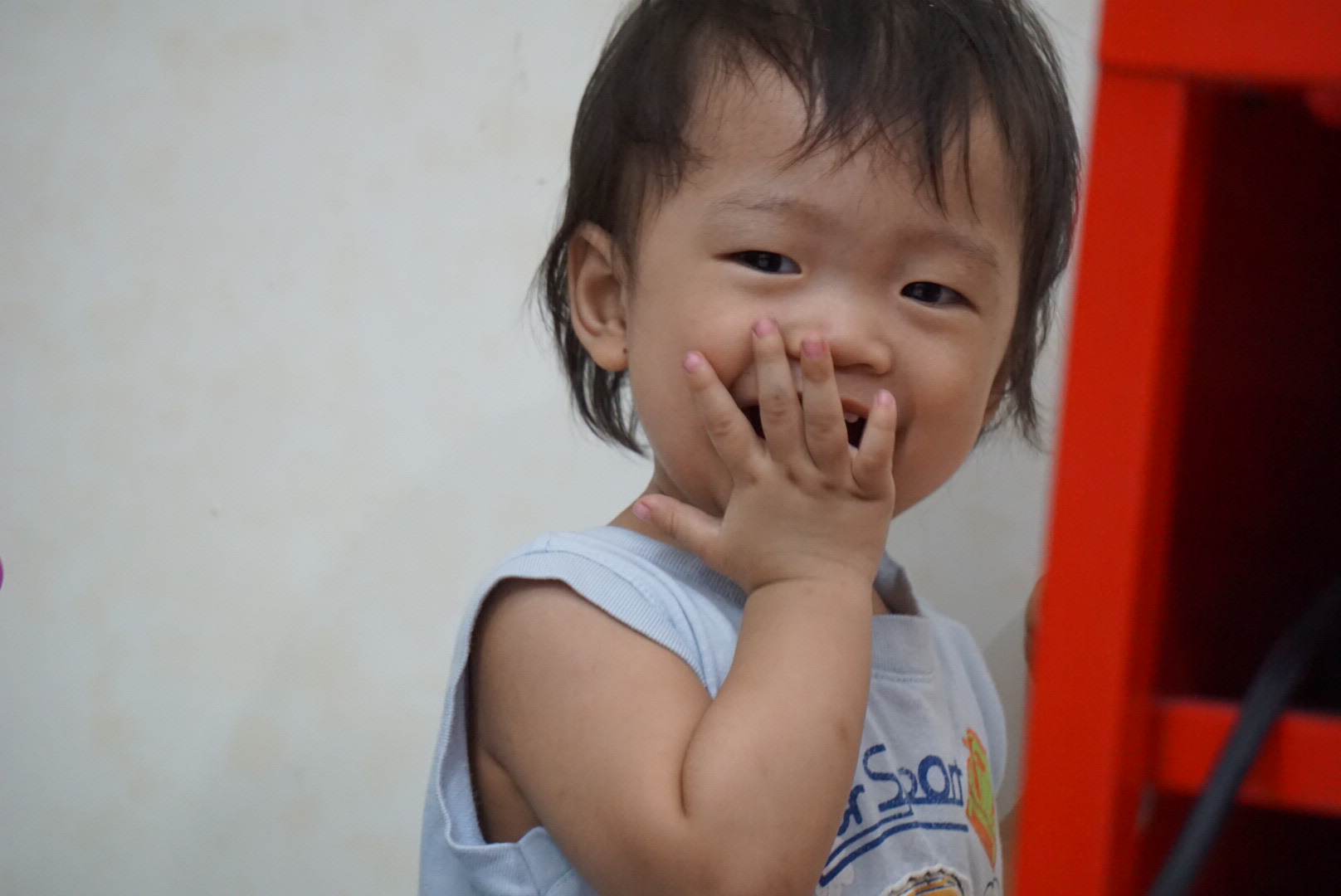 a child smiles while putting his hands on her mouth