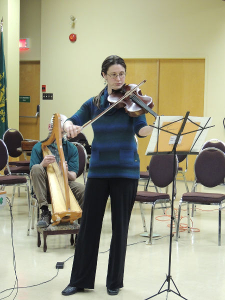 a woman playing a violin while people sit in chairs in the background