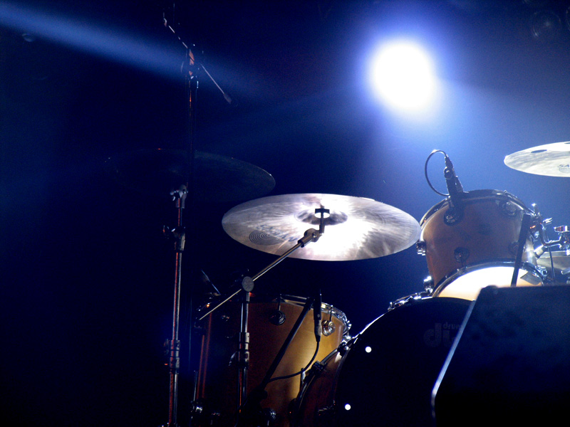 a musician playing drums on stage with light streaming from behind