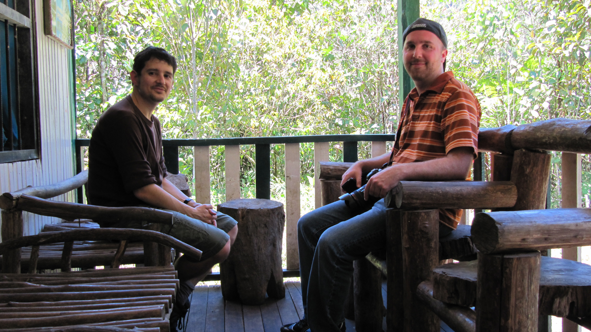 two men sitting on a porch with wooden posts