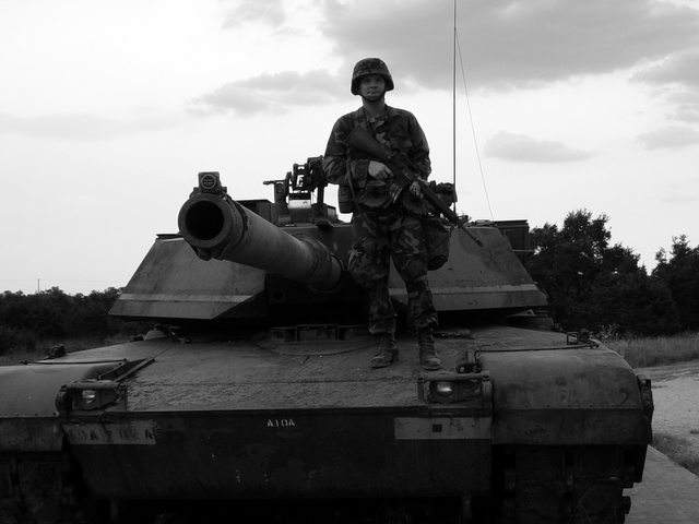 military person in camouflage standing on top of an old tank
