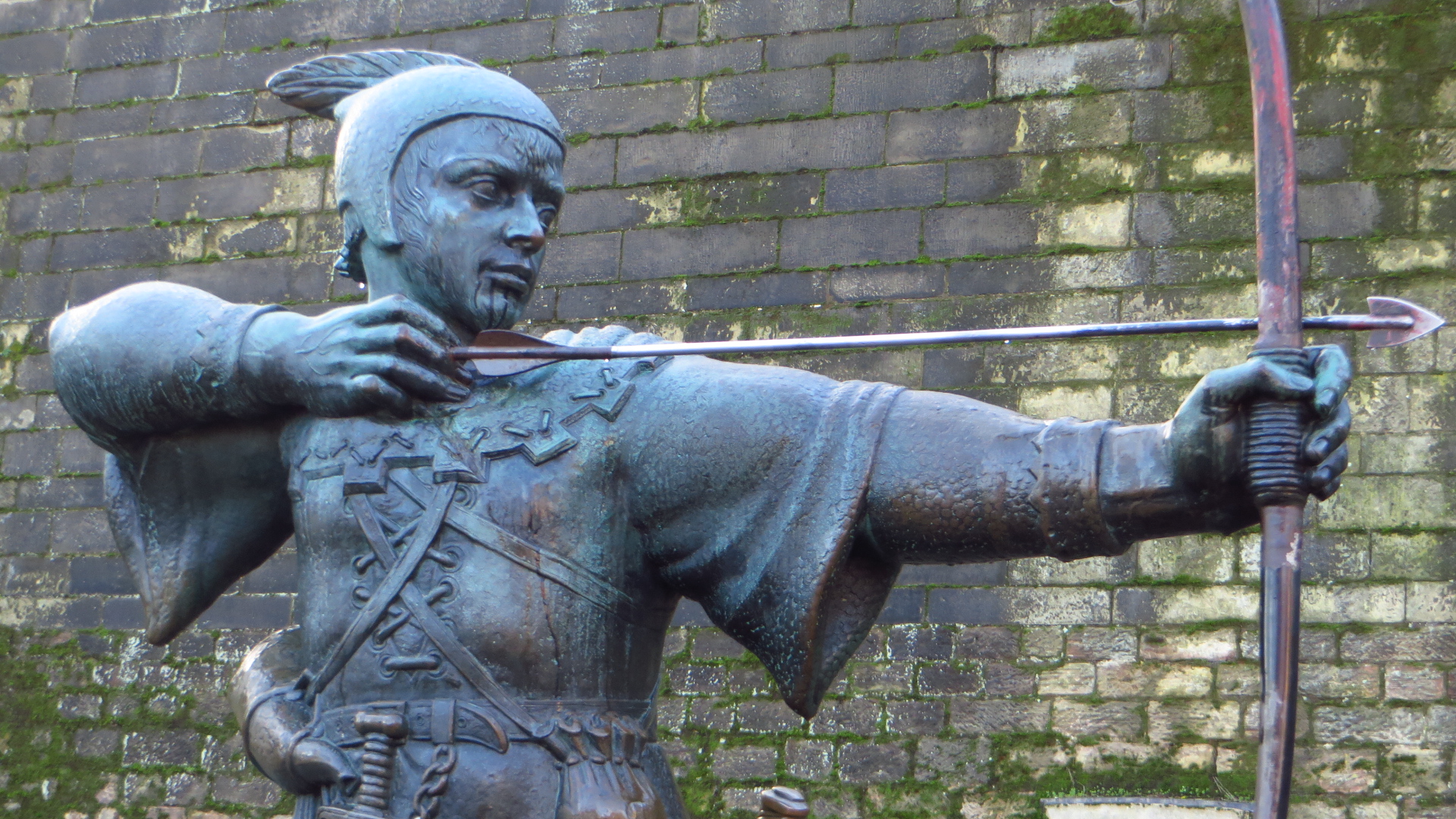 the statue in front of a brick wall is holding a spear