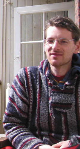 the man is sitting down wearing glasses, a striped sweater and jeans