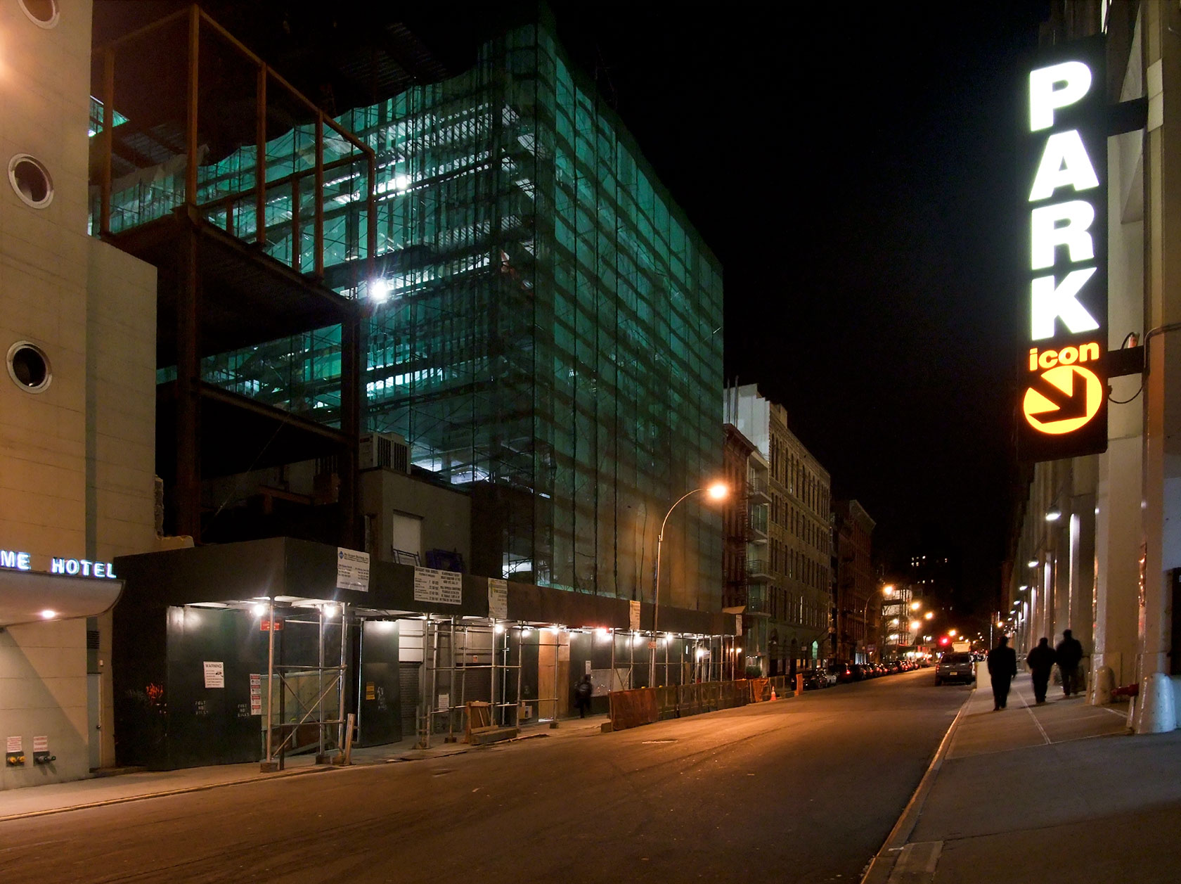 people walk down the side of a narrow city street at night