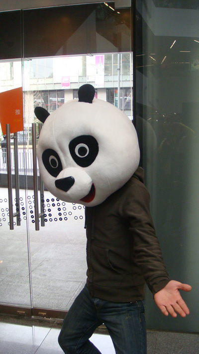 a man walking past a giant panda bear mask on display