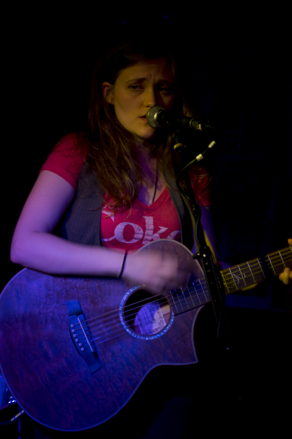 a woman holding an acoustic guitar at a microphone