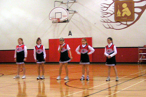 young cheerleaders stand in formation on a gymnasium basketball court
