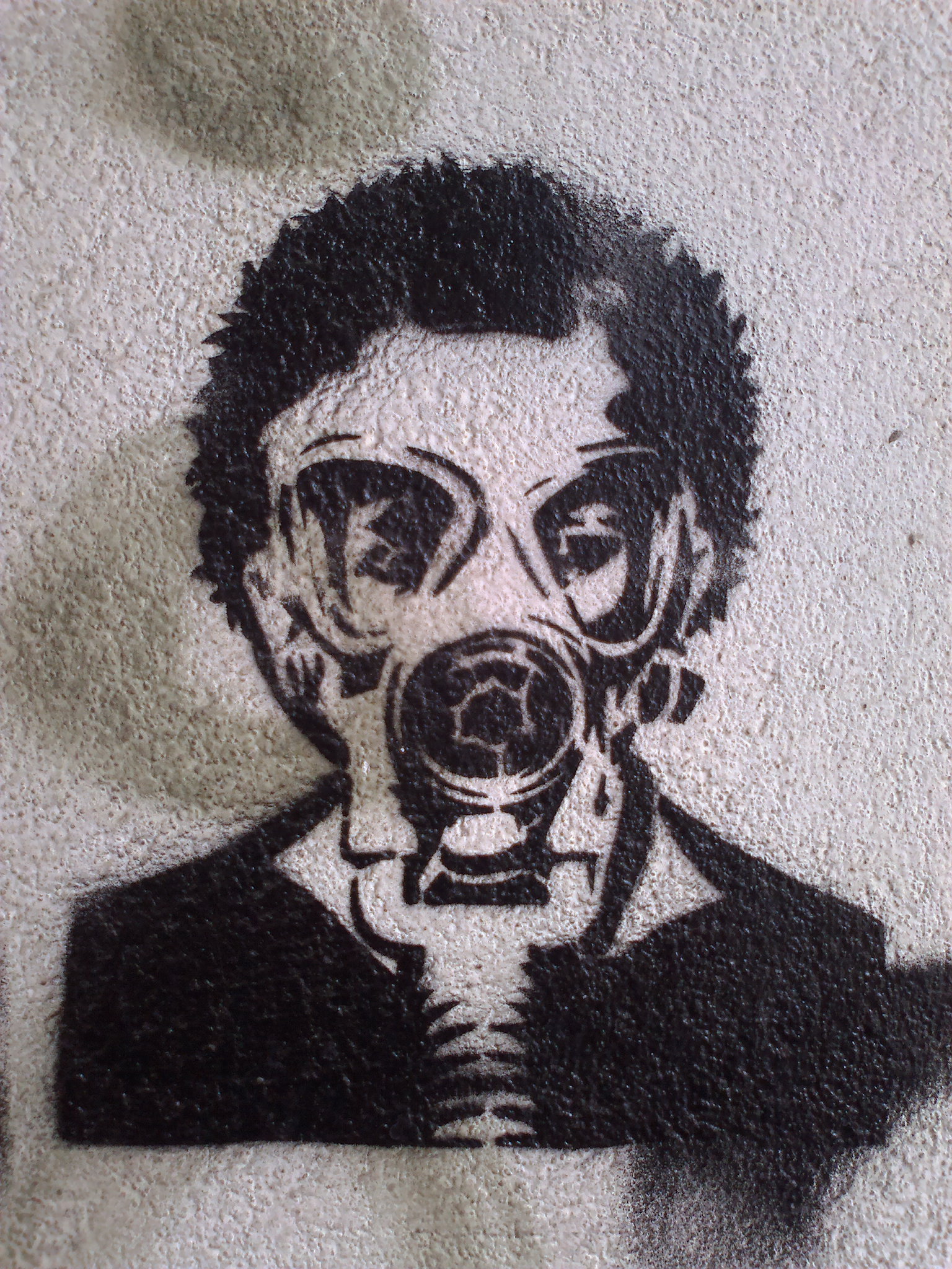 a man in a gas mask and jacket standing next to graffiti