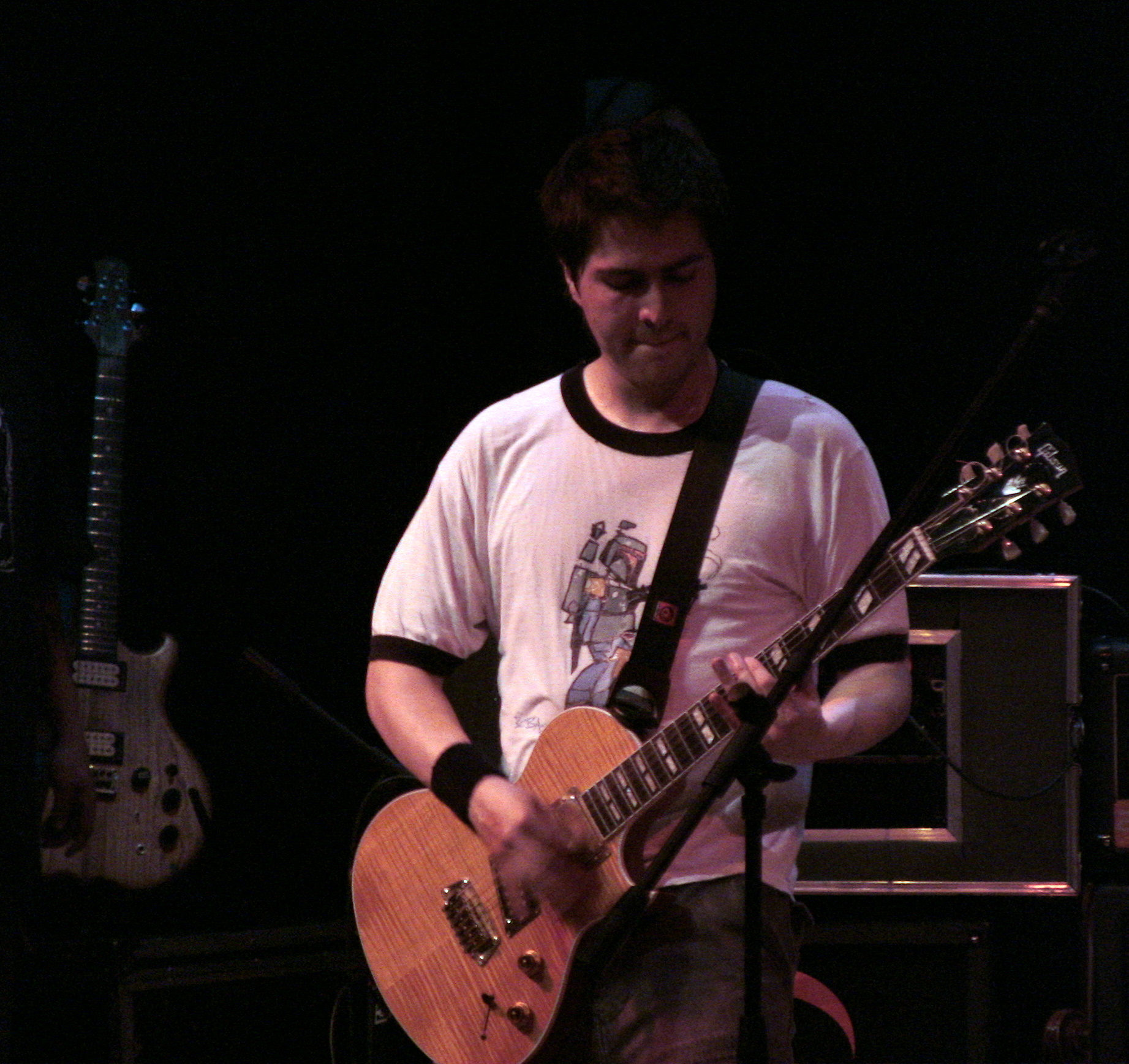 man in white t - shirt with guitar in front of microphone