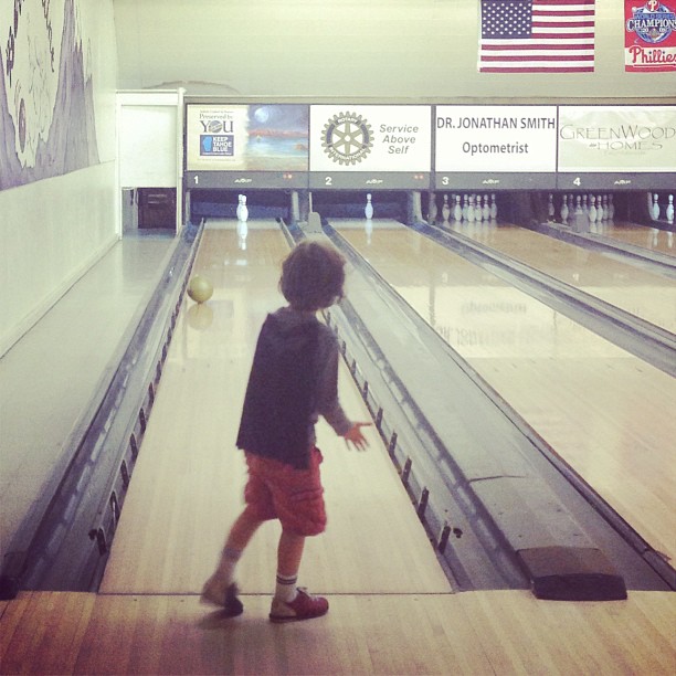 a little boy who is riding on a bowling court