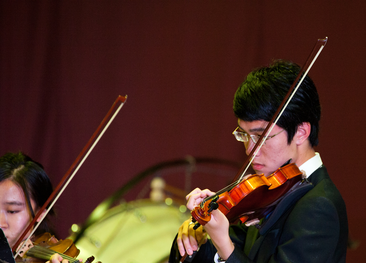 two asian men playing violin together in front of an audience