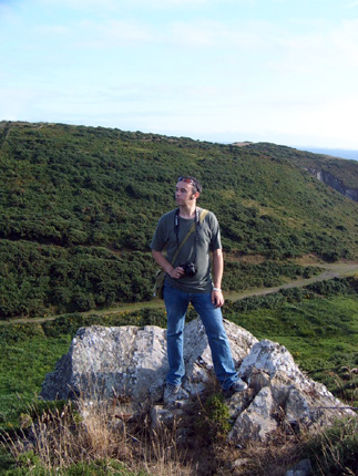 a man is standing on a large rock on a grassy hill