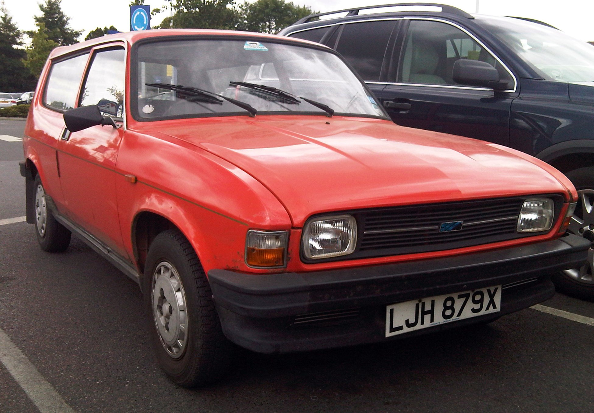 red car parked in a lot next to black vehicles