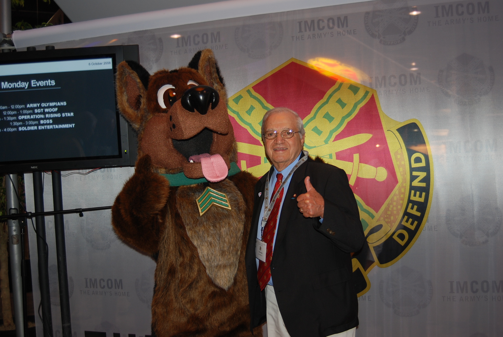 a man poses with a large brown mascot and television