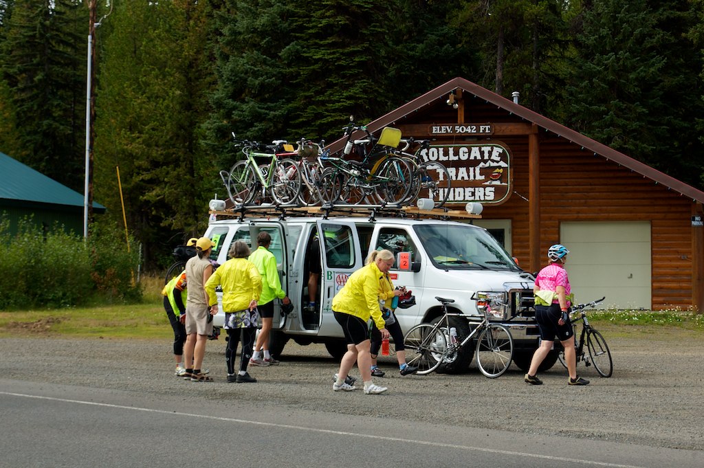 three people are walking in front of a van carrying bikes