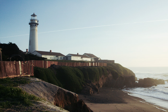 light house by the water near a beach and rocks