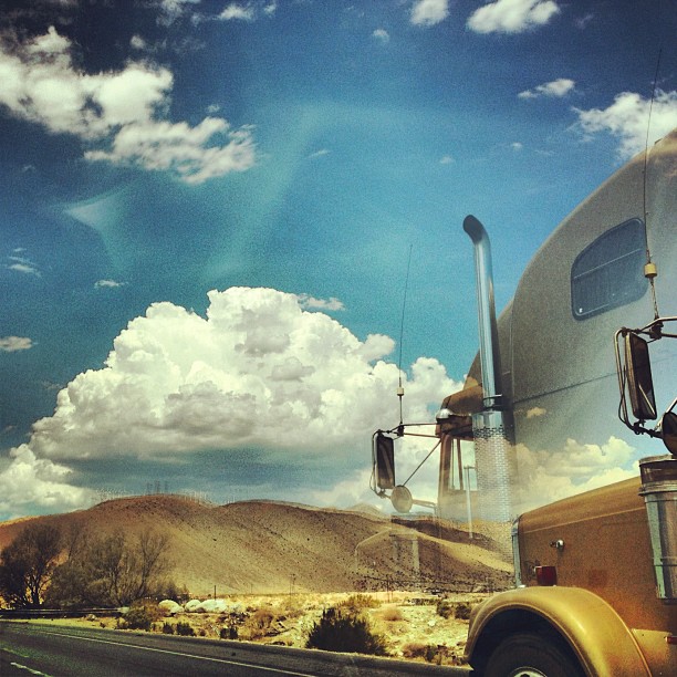 a yellow truck drives on the highway with mountains in the background