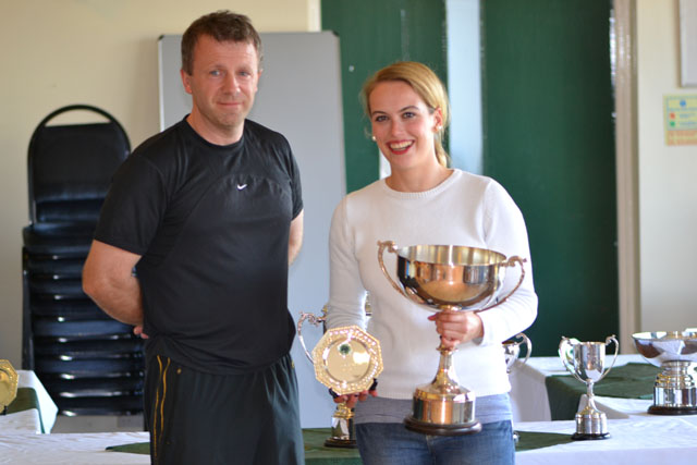a woman holding two trophies and standing next to a man in black