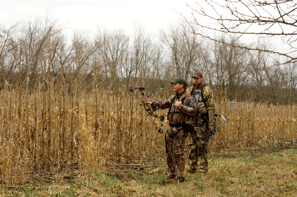 two men in camouflage standing in a field with an bird