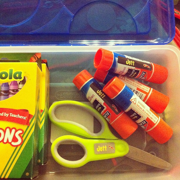 some scissors are on a plastic container next to glue and pens