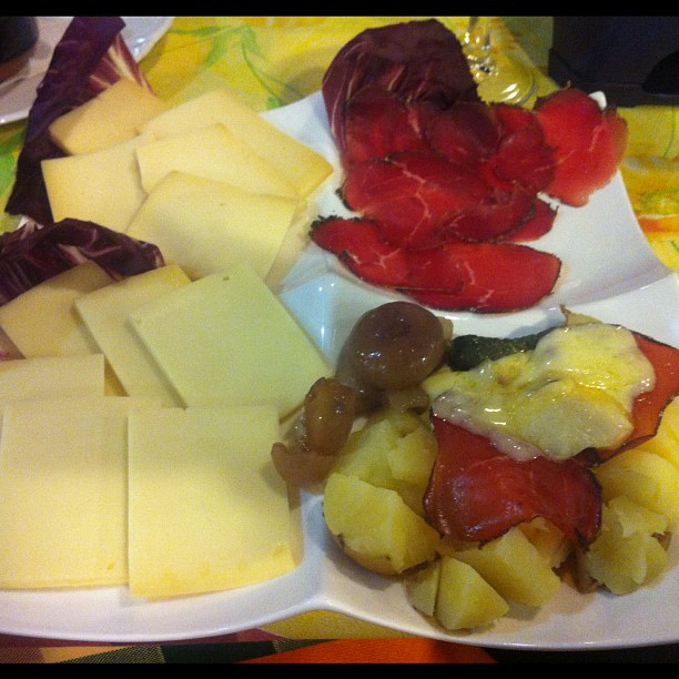 cheeses, fruit and meat are arranged on separate plates