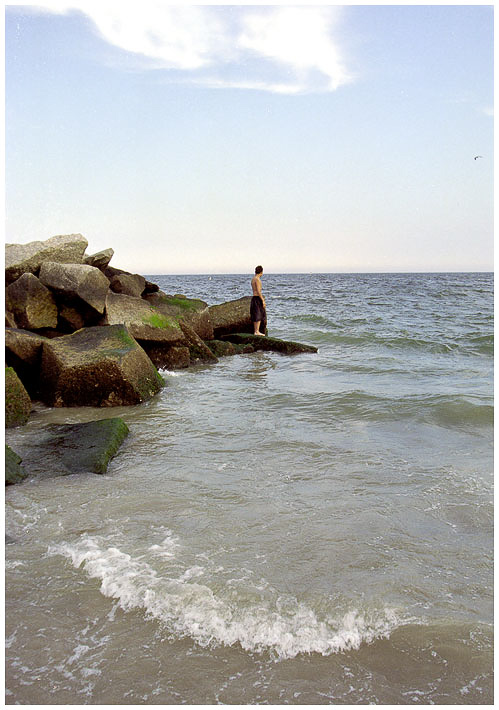 a person that is standing on rocks by the ocean