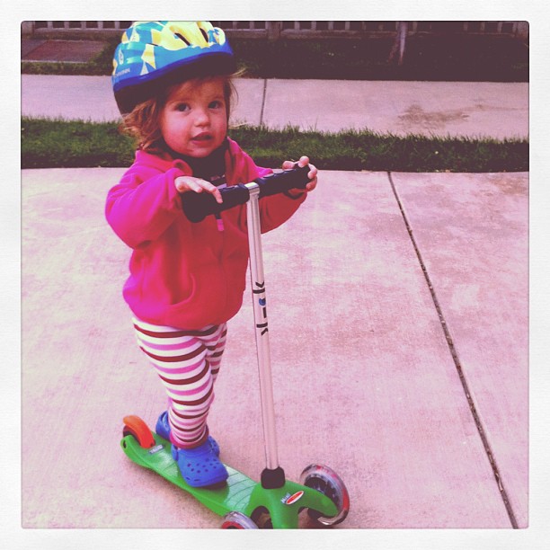 a toddler with a helmet riding on a scooter