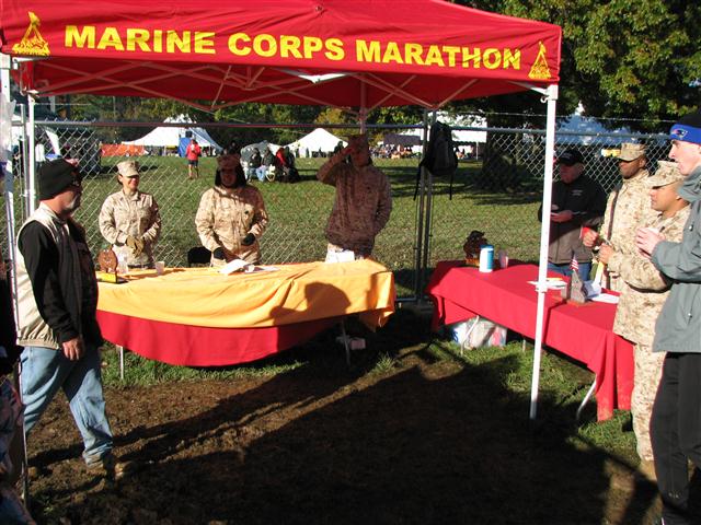 military personnel stand at a red tent with a yellow table cloth
