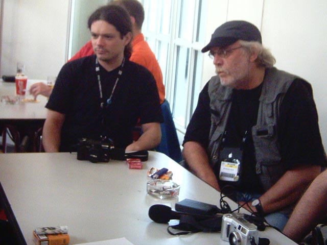 two men sitting at a table with one holding a camera