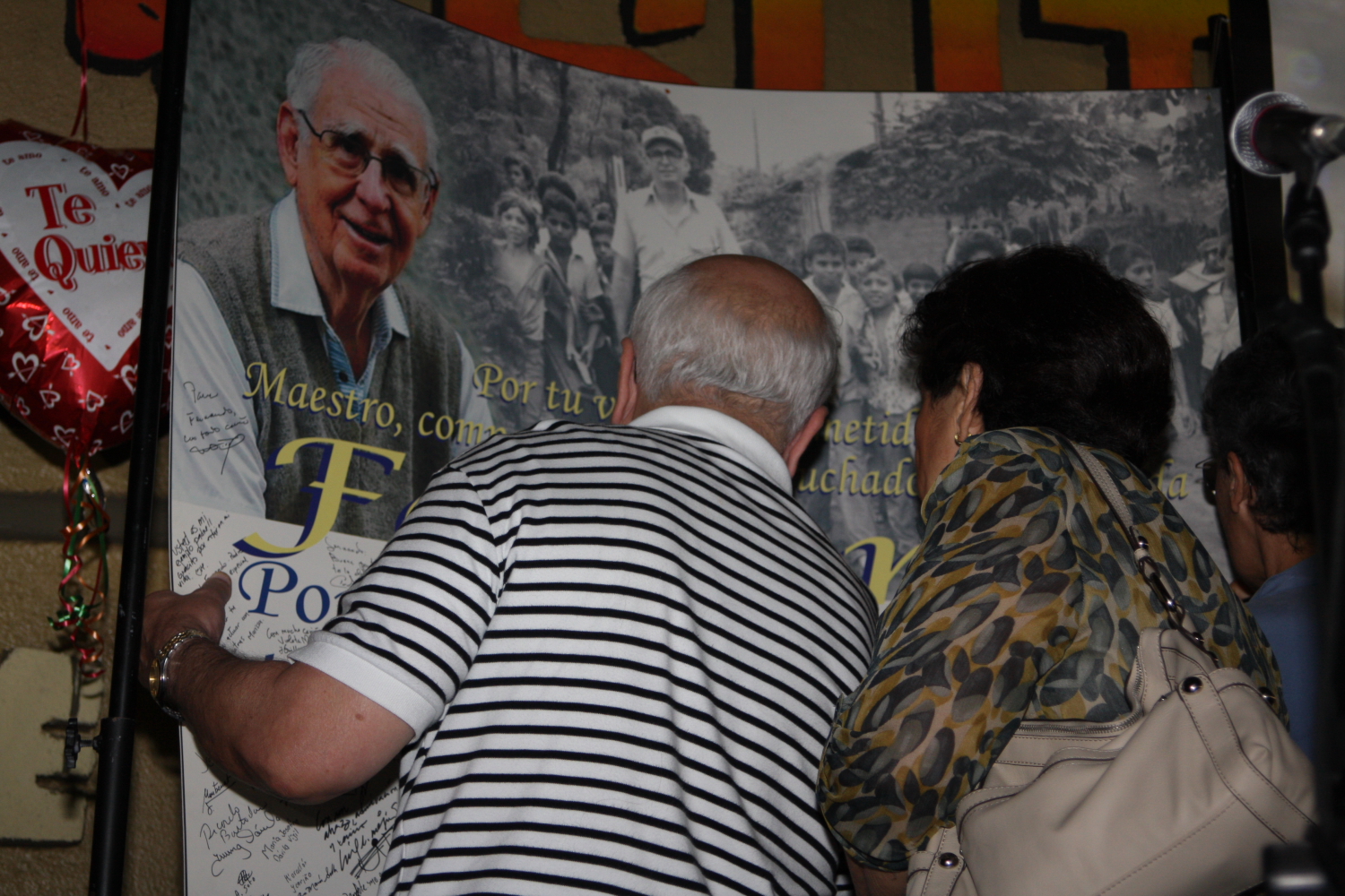 two people look at a sign of an older man in front of the poster