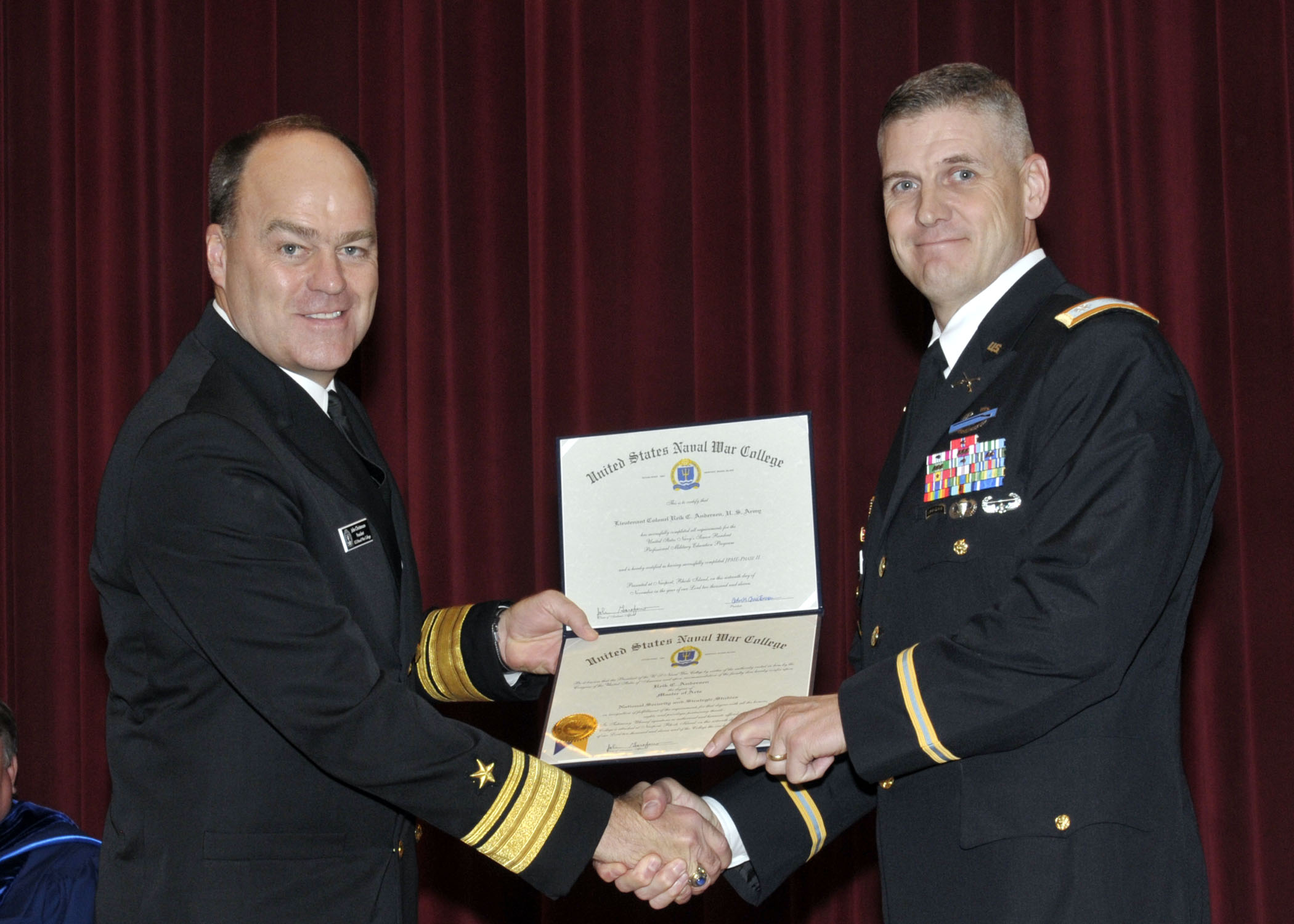 two men in military uniforms shaking hands while one man wearing uniform is holding a certificate