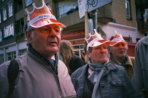 an old man standing on a street with many people wearing orange hats