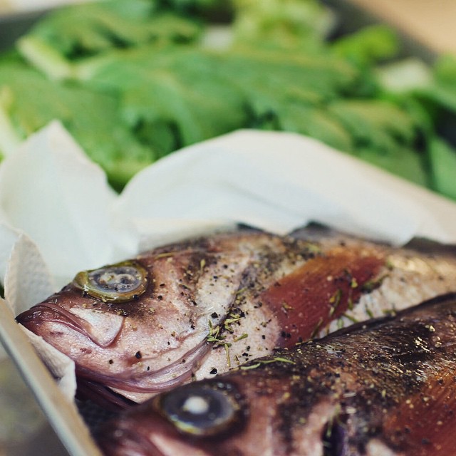 raw fish sit on a tray beside a plate with broccoli