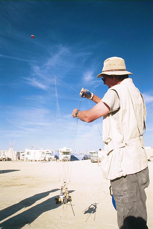 man in white shirt with hat flying his kite