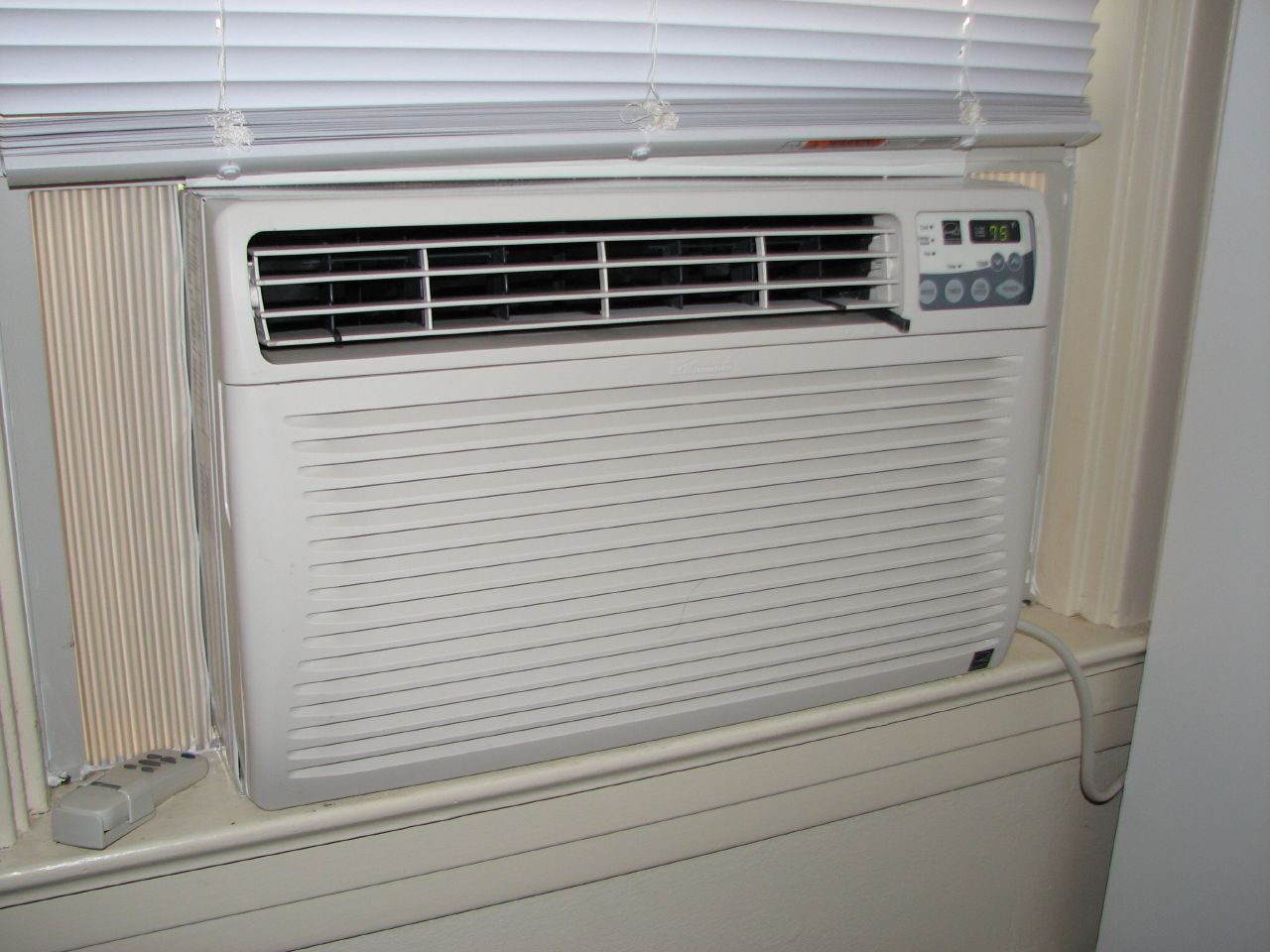 air conditioner sitting in a window sill with windowsill and blinds
