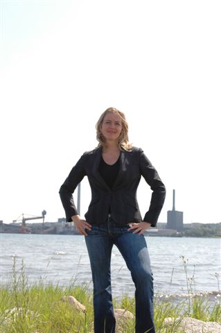 a woman in jeans and jacket stands in front of the water