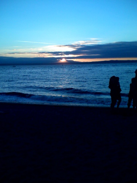 two people walk along a beach as the sun goes down