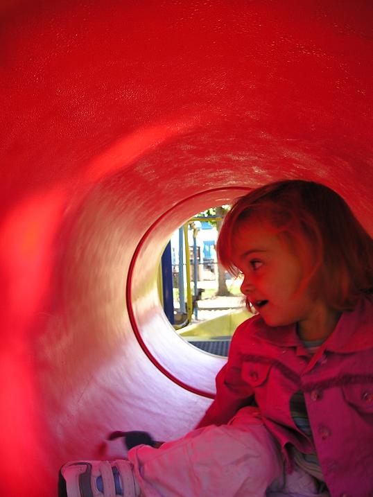 a little girl sitting in a tube in the playground